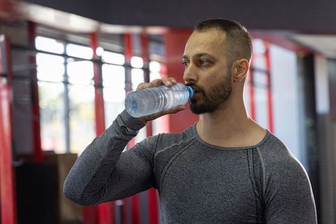 Indian man drinking water after boxing training in gym wearing fitted grey top