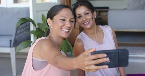 Two women taking selfie together in living room wearing sleeveless pastel athletic tops
