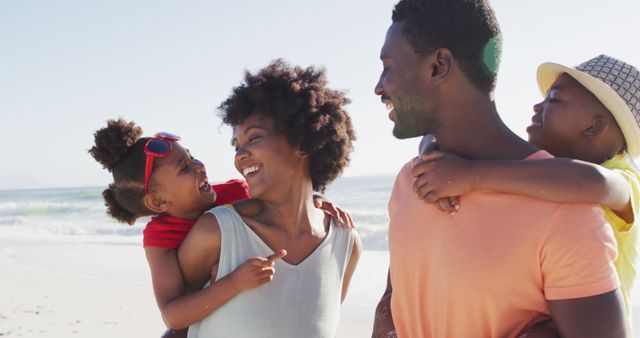 Smiling african american family carrying and embracing on sunny beach. healthy, active family beach holiday.