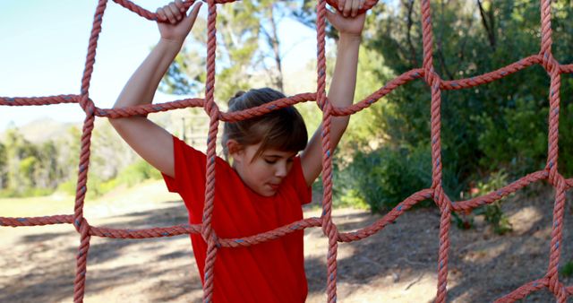 Boy holding onto outdoor climbing net in sunshine, engaging in active play. Perfect for use in content about children's outdoor activities, playgrounds, exercise, and healthy lifestyles for kids.