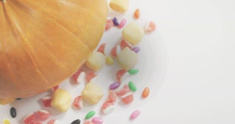 Pumpkin resting among colorful candy on white minimal background for autumn halloween layouts