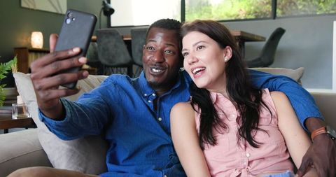 Happy Interracial Couple Video Calling on Sofa Celebrating Engagement