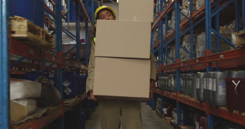 Warehouse Worker Carrying Stacked Boxes Between Shelves
