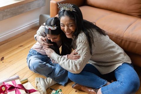 Mother and daughter hugging on sunlit floor with wrapped gifts, cozy family moment