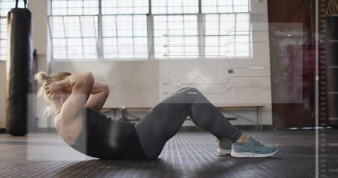 Woman doing crunches in sunlit studio gym with teal sneakers and punching bag, core training