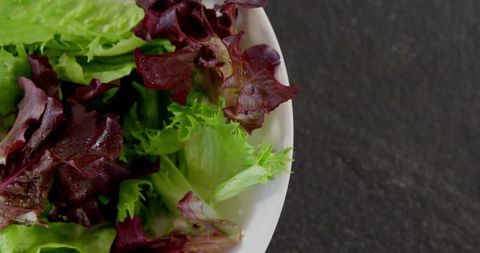 Assorted fresh lettuce leaves in white bowl on stone countertop