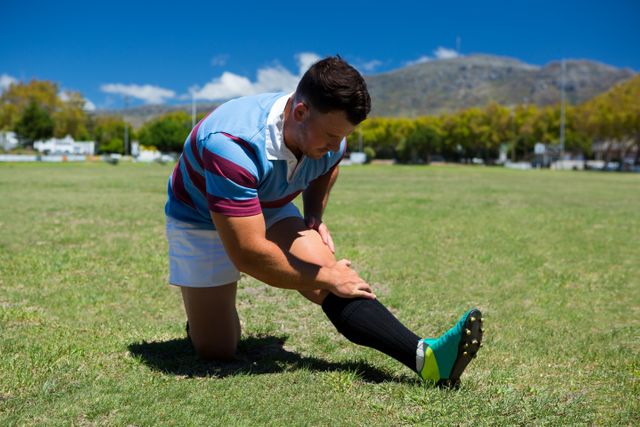 Young rugby player stretching on grassy field on sunny day. Ideal for use in sports and fitness articles, athletic training programs, outdoor activity promotions, and health and wellness blogs.