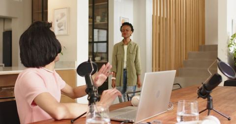 Recording podcast with cohost in modern home studio, woman in pink pearls using laptop
