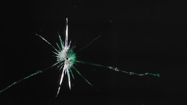 Close-up view of shattered glass against a black background highlighting vivid cracks and damage. Useful for illustrating concepts of risk, safety, accidents, and impact. Ideal for use in safety presentations, dramatic backdrops, and digital interfaces representing damage or instability.