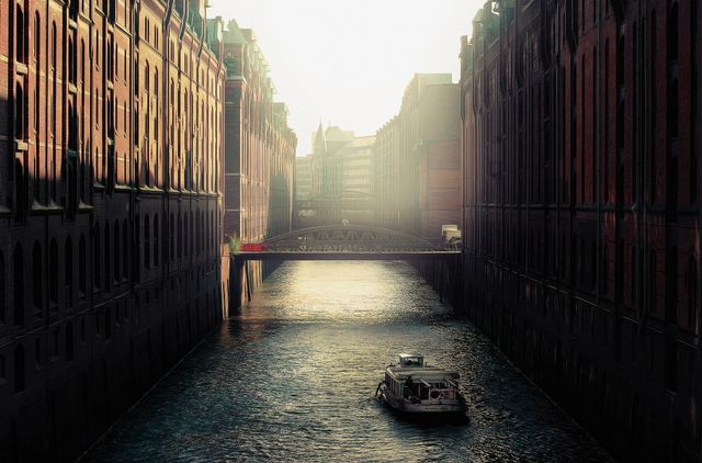 Boat traveling through urban canal surrounded by historic buildings during sunset. Soft light creates tranquil atmosphere perfect for travel, urban exploration, and historic themes. Ideal for blogs, websites, marketing materials related to city living, tourism, or cityscape photography.