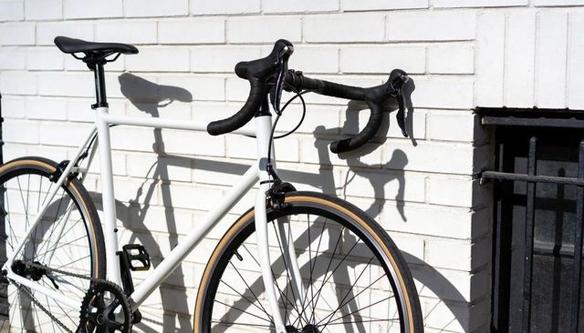 Leaning white road bike casting crisp shadows on sunlit brick wall