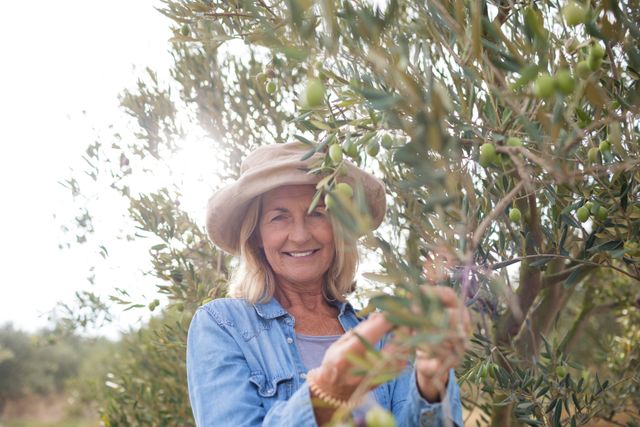 Portrait of happy woman harvesting olives from tree in farm
