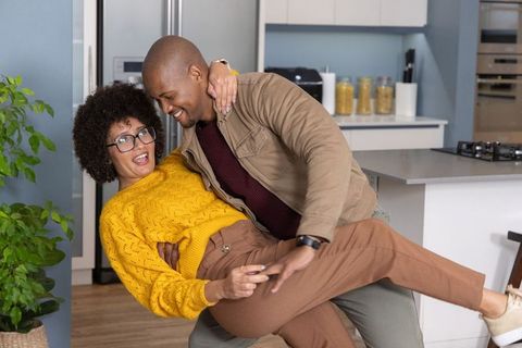Diverse couple dancing and laughing in modern kitchen while man lifting partner playfully