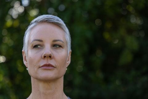 Reflective middle-aged woman standing in garden with short gray hair and stud earrings