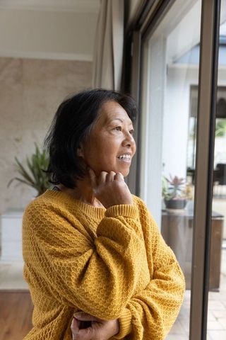 Senior Woman Contemplating by Window in Warm Sweater Indoors