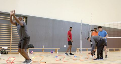 Diverse men practicing agility drills in gymnasium with hurdles volleyball team training