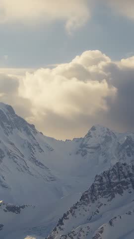 Drifting cumulus cloud moving over snow-covered alpine valley under soft golden light