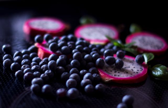 Slices of dragon fruit and scattered blueberries, highlighting the vibrant colors and textures of these fresh, nutritious fruits. Perfect for illustrating healthy eating habits, antioxidants benefits, nutritious diet concepts, or recipes featuring tropical and exotic fruits.