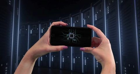 Hands holding smartphone showing microchip circuitry against neon-lit data center racks