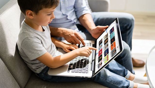 Father and son browsing videos on laptop, pointing at screen, sharing digital learning