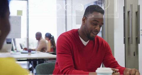 Man in red sweater reading document in modern open-plan coworking office with coffee cup