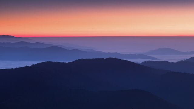 Panoramic view of mountain ridges silhouetted against dawn sky, with misty valley below. Ideal for background images, nature magazines, travel brochures, or wall art aimed at showcasing serene natural landscapes and tranquil atmospheres.