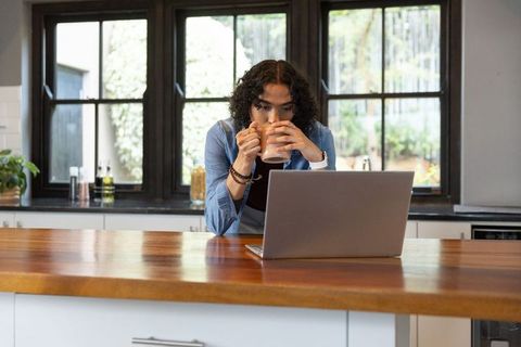 Non-binary person working remotely at kitchen island with laptop and morning coffee home office life