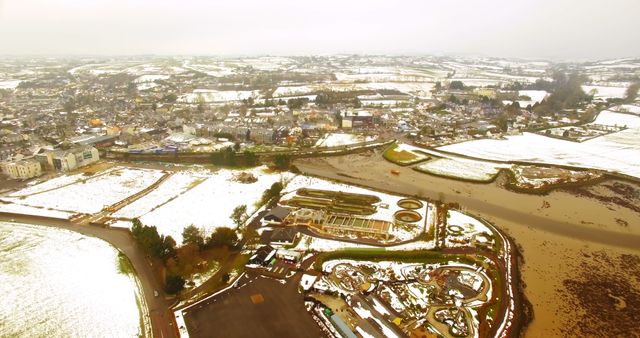 Aerial view capturing the essence of a small town and its surrounding snow covered farmlands in the countryside. Mixed landscapes featuring residential areas, intricate water pathways, and plots of land add depth and detail. Ideal for use in articles or projects about winter, rural living, countryside landscapes, weather patterns, or seasonal changes.