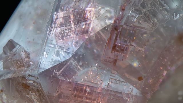 Iridescent clear crystal macro revealing faceted inclusions, fractures and reflections