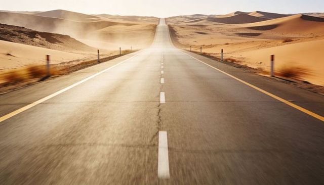Stretching desert highway receding to horizon through golden sand dunes, empty remote road