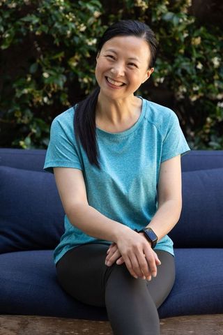 Middle-aged east asian woman relaxing on garden sofa wearing smartwatch and teal top