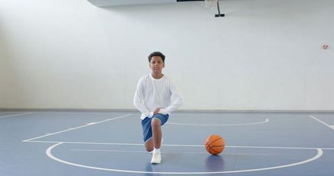Young Athlete Kneeling on Basketball Court Holding Ball