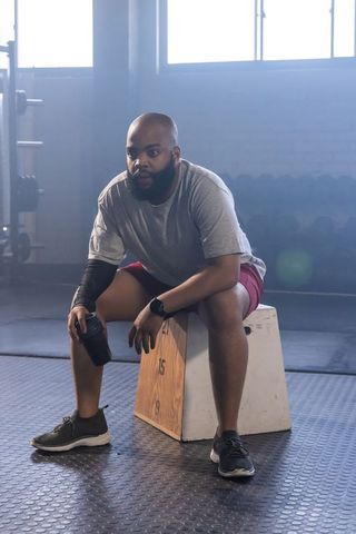 African man resting after high intensity workout sitting on plyo box holding shaker