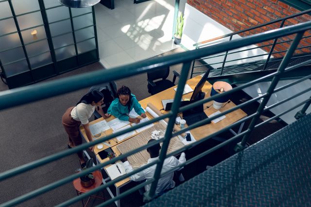 This image can be used for articles or blogs about teamwork, business strategies, and modern office environments. It is also suitable for corporate presentations or websites showcasing professional and collaborative workspaces. The high angle view adds a unique perspective, emphasizing the dynamics of group work in a creative setting.