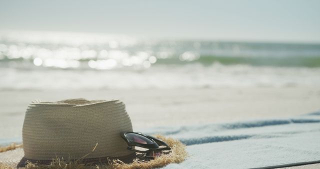 Straw hat and sunglasses laying on a sandy beach with ocean waves in the background. This image evokes feelings of relaxation, summer vacations, and enjoying sunny days by the sea. Perfect for travel promotions, vacation advertisements, or summer-themed content.