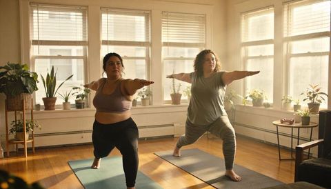 Practicing warrior ii pose during sunny at-home yoga session with two women on mats