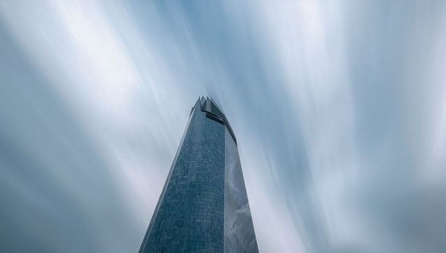 Soaring angular glass skyscraper with crown slit and streaked cloud motion