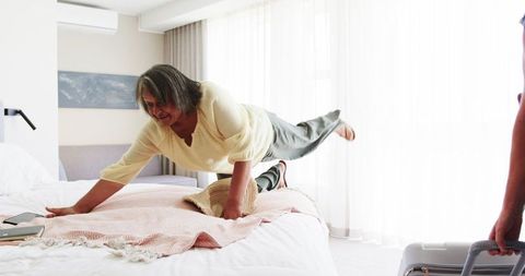 Playful Senior Woman on Bed with Traveler in Modern Home