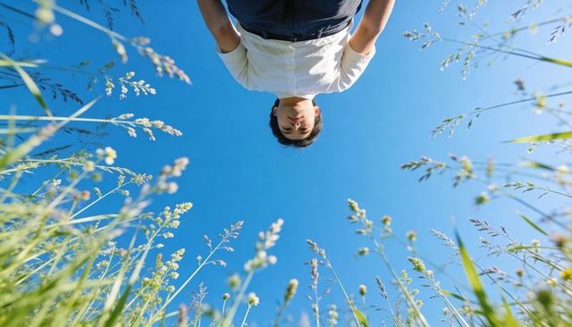 Worms-eye portrait young man leaning over meadow of tall grass under vivid blue sky