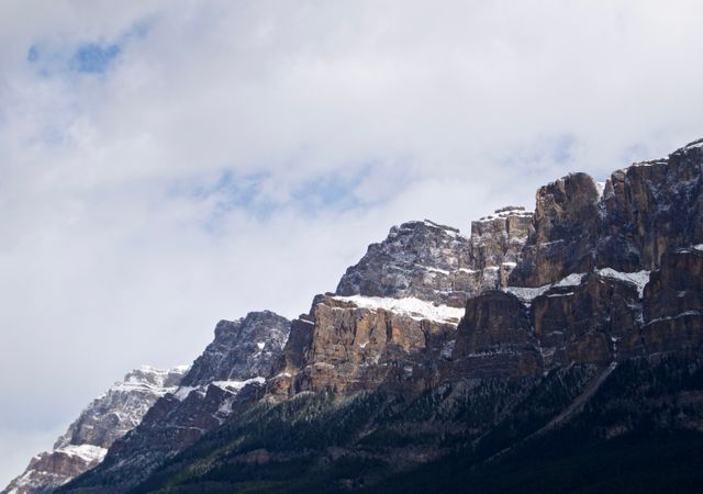 Snow-capped rocky mountain peaks set against a cloudy sky. Perfect for use in travel brochures, nature documentaries, scenic posters, and outdoor adventure marketing materials. Captures the essence of untouched wilderness and natural beauty.