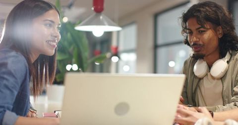 Diverse coworkers collaborating, smiling, discussing project on laptop in coworking space