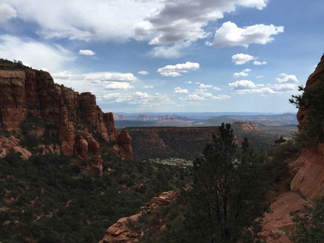 This image captures a stunning view of majestic red rock cliffs framing a distant mountain range under a partly cloudy sky. Ideal for travel brochures, adventure blogs, or nature-themed websites. Perfect for promoting outdoor activities like hiking or exploring scenic landscapes.