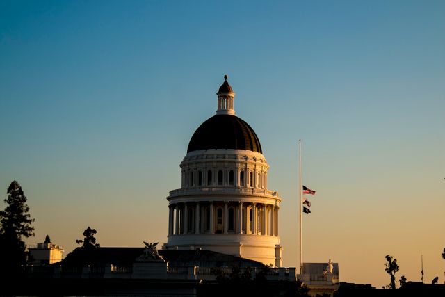 Capitol building dome is silhouetted against a serene evening sunset. Ideal for depicting government, politics, or solemn events. Suitable for articles on governmental structures, architecture, or special state events and memorials.