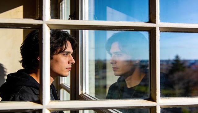 Young man gazing through multi-pane window with reflective profile and contemplative mood