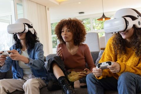 Diverse Women Playing Virtual Reality Games on Sofa at Home with Controllers and Snacks