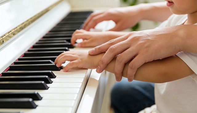 Parent guiding child hands on piano keys during home music lesson sunlit close-up