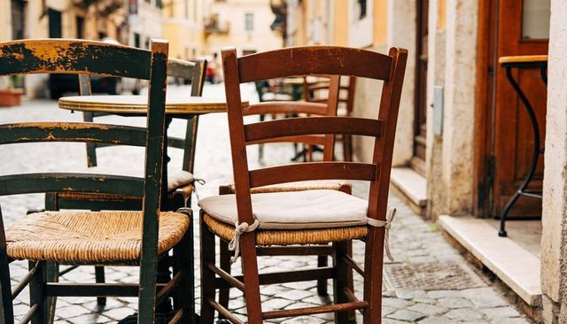 Rustic italian cafe chairs on cobblestone alley featuring tied beige cushion and patina