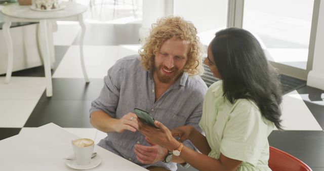 Happy diverse couple with coffee using smartphone and talking at a table in cafe - Download Free Stock Photos Pikwizard.com