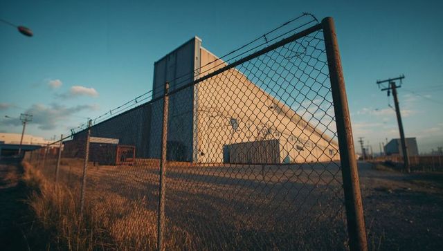 Industrial Warehouse Behind Barbed Wire Fence at Sunset