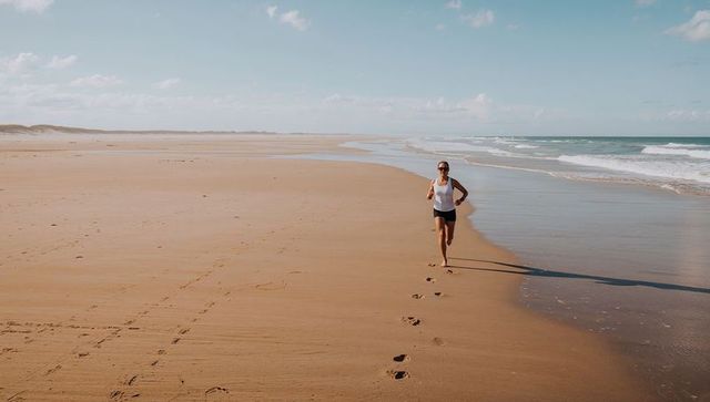 Solo woman running barefoot along vast sunrise beach leaving footprints on wet sand